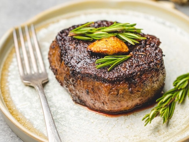 filet mignon on plate with rosemary sprig and fork